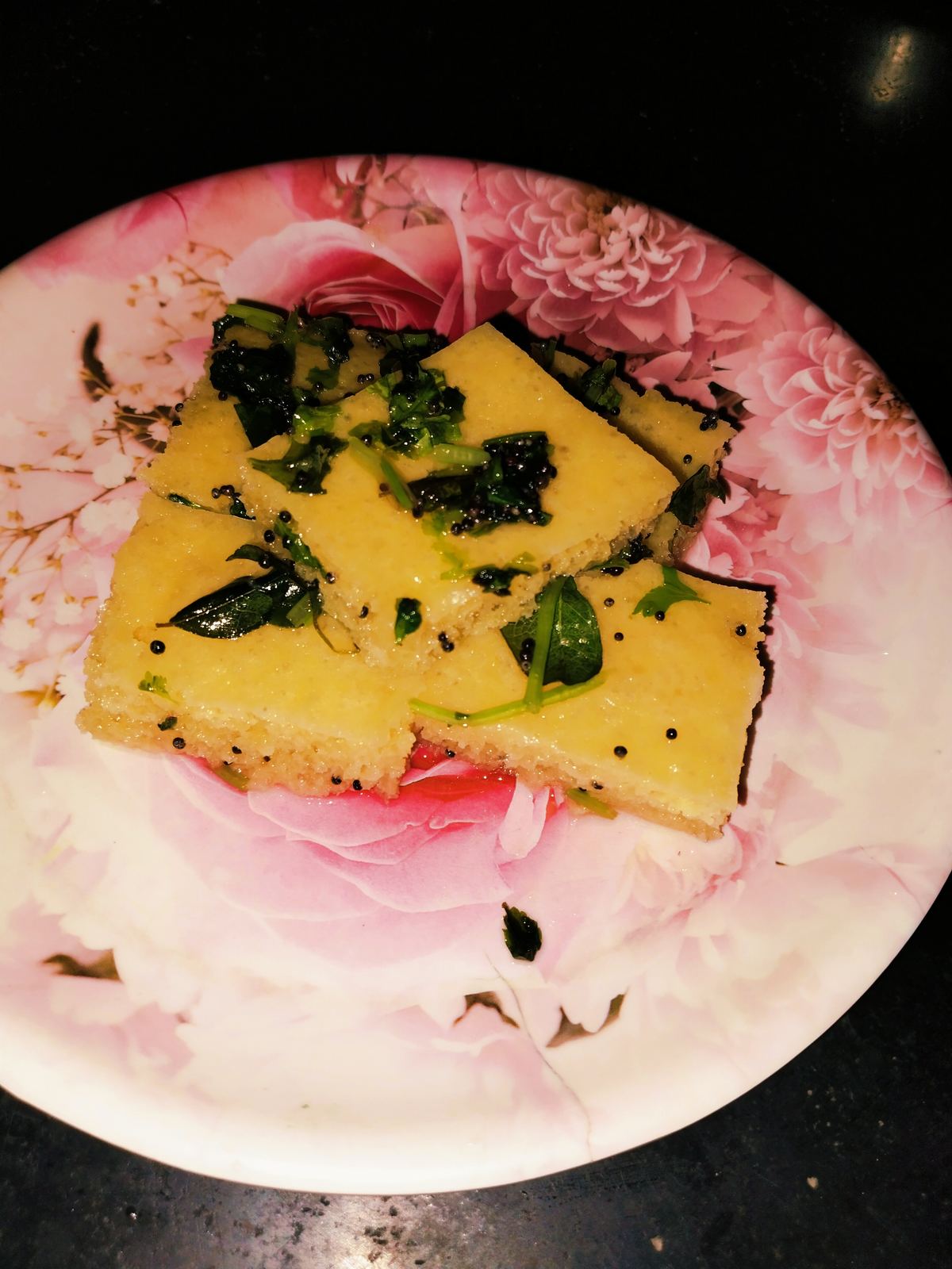 Top-down photo of steamed Khaman Dhokla garnished with coriander and mustard seeds