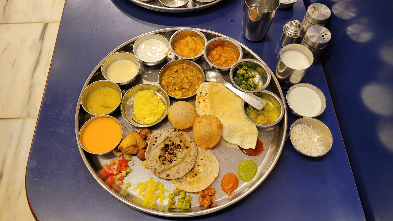 Steel thali with rice, kadhi, and rotli on a floral tablecloth